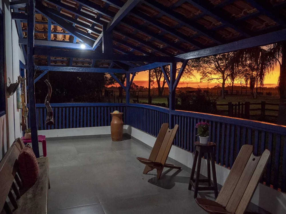 Wooden chairs rest on the blue-painted veranda of the historic Pequi farmhouse lodge during a vibrant Pantanal sunset. 