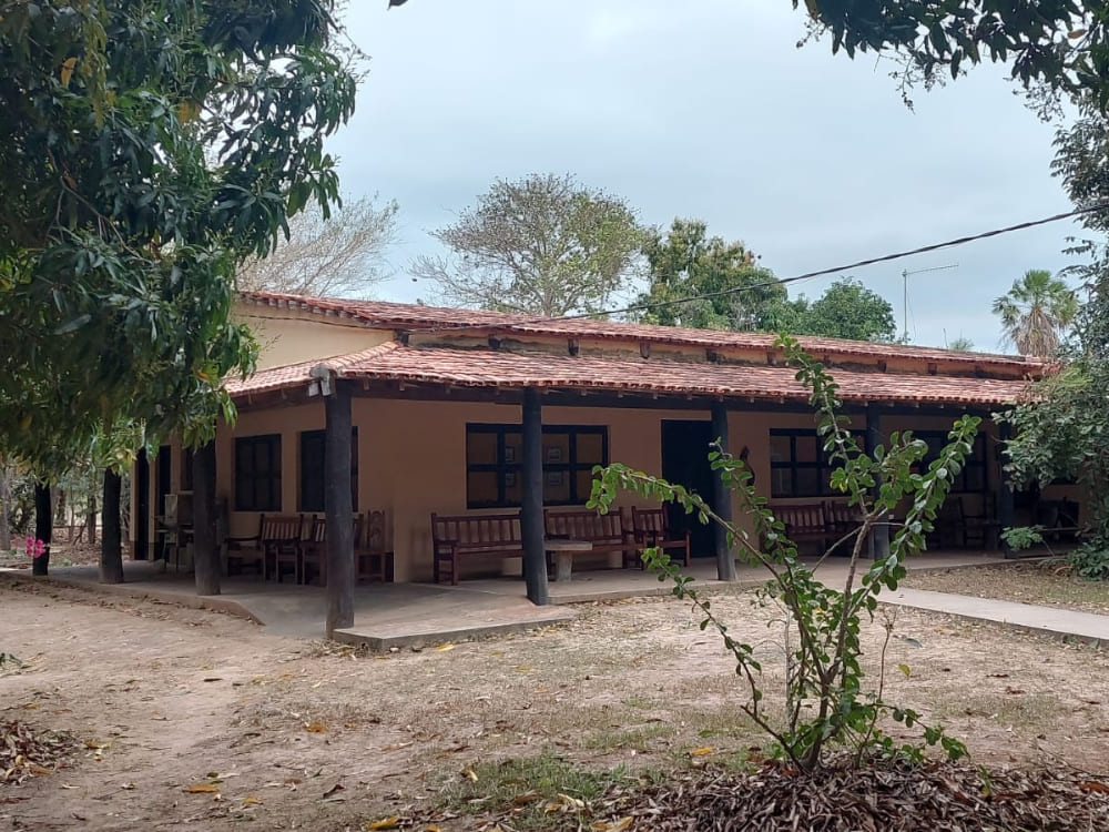The simple and functional rustic farm architecture of Pouso Alegre lodge is shaded by large green trees.