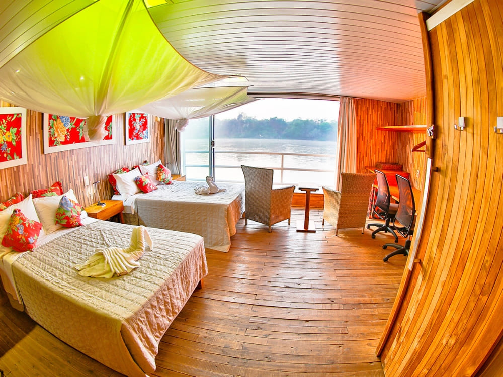 A comfortable cabin inside the Southwild Flotel features two beds, wooden floors, and a large window overlooking the river.