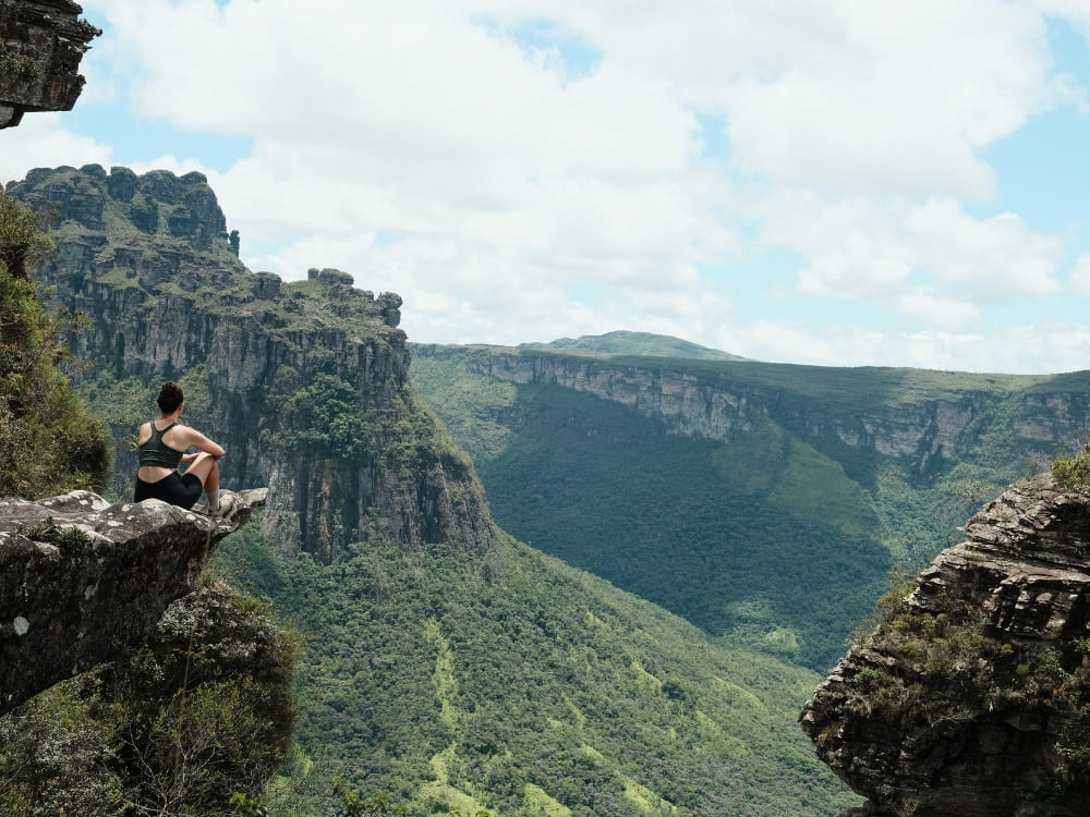Hiker sitting on a rocky cliff overlooking the green canyons of Chapada Diamantina National Park in Brazil. 