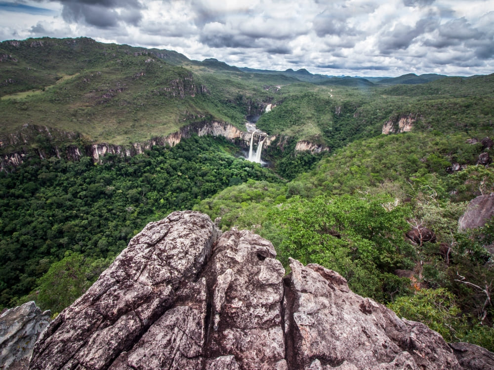 View from a rocky overlook showing a distant waterfall and lush vegetation in Chapada dos Veadeiros National Park. 