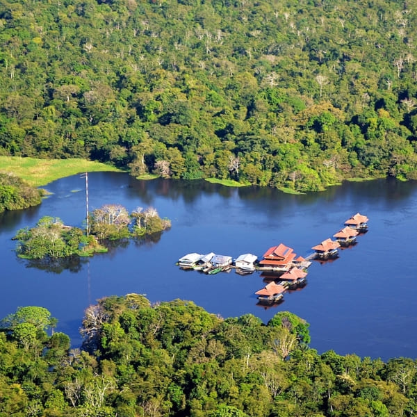 Aerial view of floating bungalows on a river surrounded by dense forest at an Amazon eco lodge in Brazil.