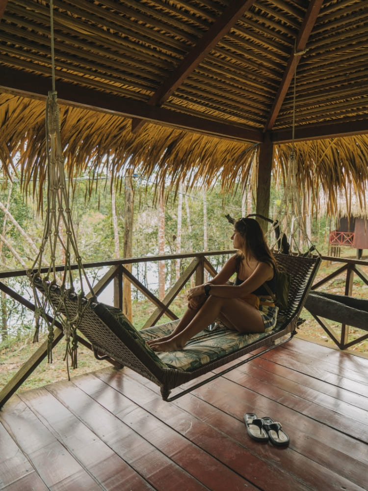 A female guest relaxes on a hanging woven hammock under a thatched roof at Amazon Turtle Lodge, a top Amazon jungle hotel.