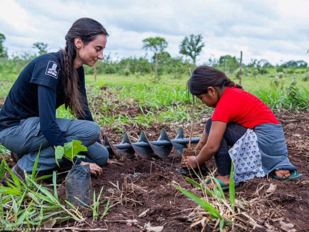 A woman and a young girl kneeling in the dirt to plant a tree sapling in the Pantanal wetlands.
