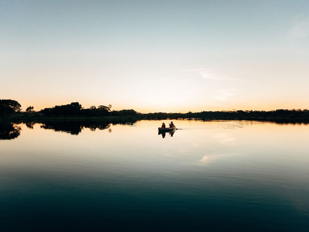 Two people paddling a canoe on a calm river that mirrors the sky in the area where is the Pantanal.