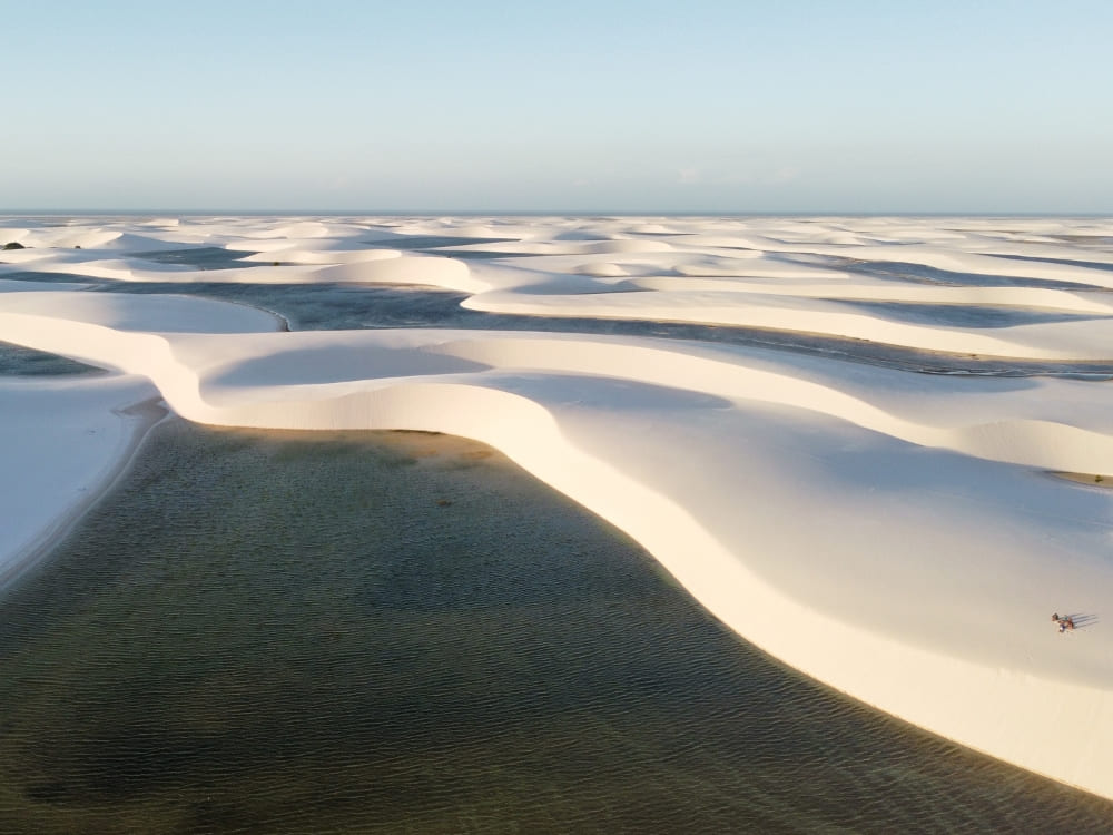 Aerial view of the active white sand dunes and rainwater lagoons in Lençóis Maranhenses, stretching toward the horizon. 