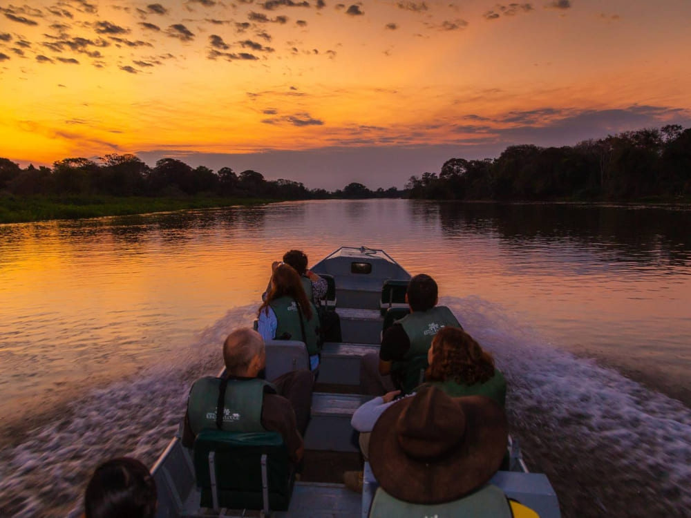 Travelers on a motorboat navigate a calm river during a vibrant orange sunset in the Pantanal Travelers on a motorboat navigate a calm river during a vibrant orange sunset in the Pantanal