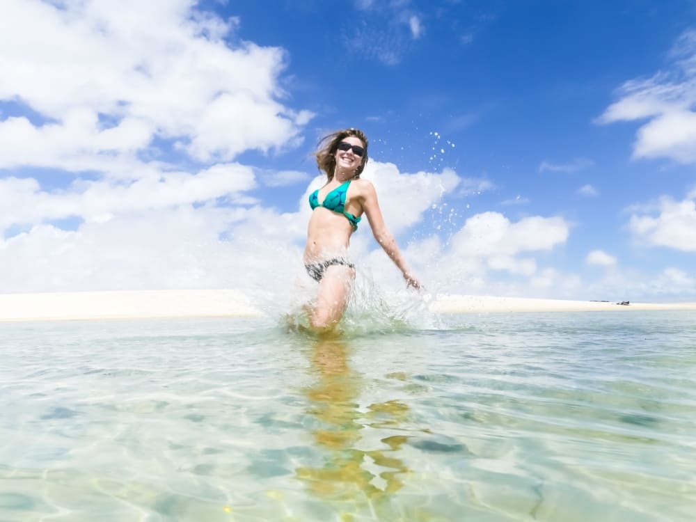 A smiling woman enjoying a refreshing swim in a crystal-clear freshwater lagoon on a sunny day in Lençóis Maranhenses.