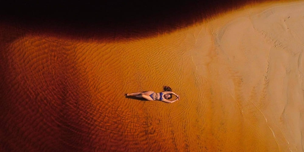 An aerial view of a woman relaxing on an expansive orange sandbank that emerges during the Amazon dry season.