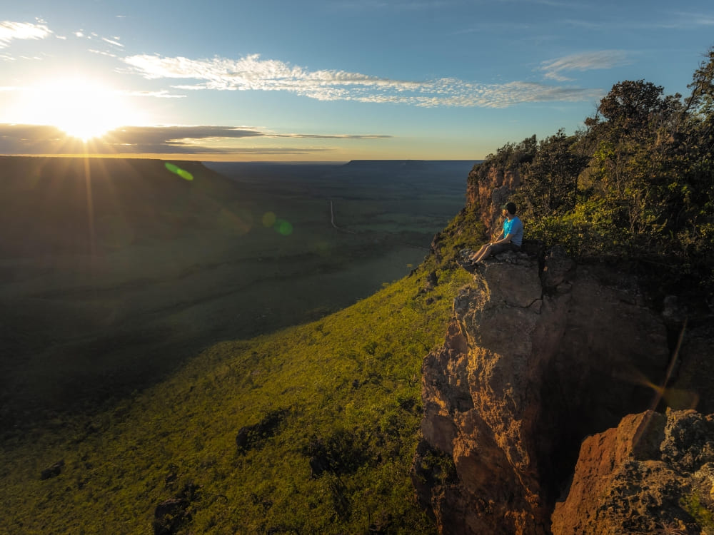 Un voyageur assis au bord d'une falaise profitant du coucher de soleil sur le vaste paysage de savane du Parc d'État du Jalapão.