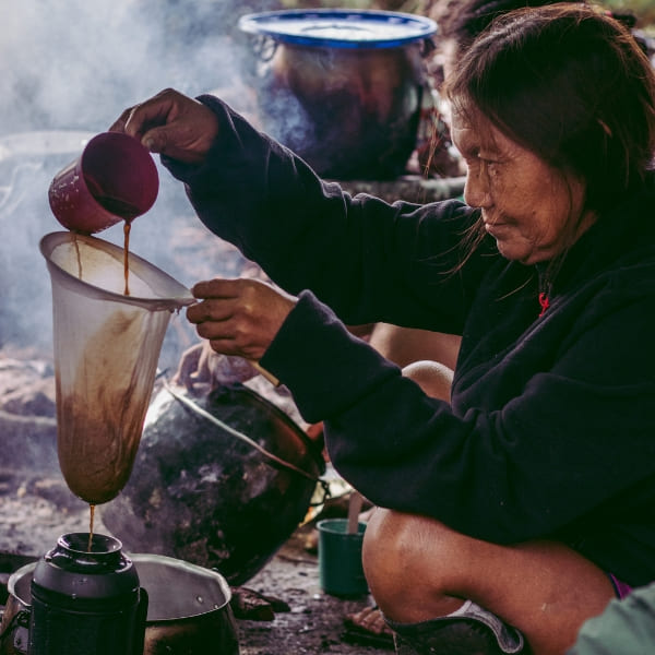 Uma mulher de uma comunidade ribeirinha local coando café em uma fogueira na Amazônia.