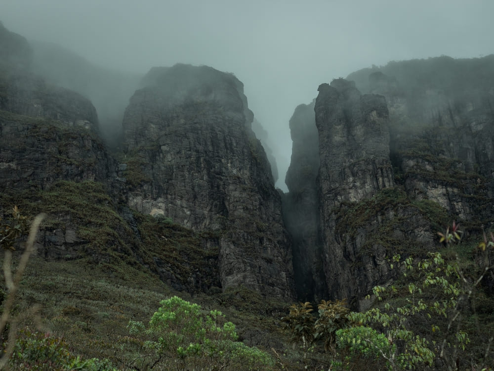 Paredões rochosos íngremes e imponentes parcialmente cobertos por uma névoa espessa no Parque Nacional do Pico da Neblina.