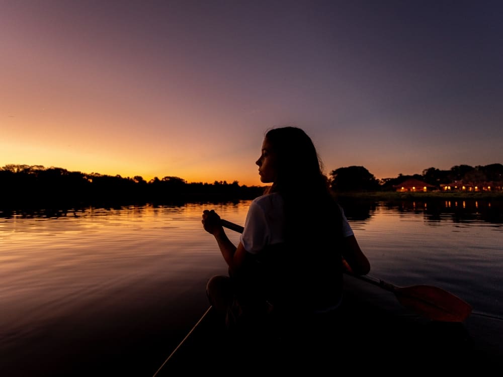 A woman paddling a canoe on a calm river at sunset, highlighting the peaceful nature of a Pantanal trip.