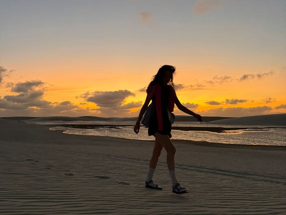 Silhouet van een vrouw wandelend op nat zand onder een schemerige lucht tijdens de beste reistijd voor het Lençóis Maranhenses national park.