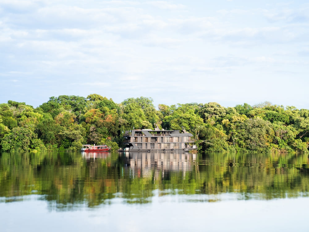 A multi-deck Amazon river cruise boat floating on calm waters reflecting the dense green forest vegetation.