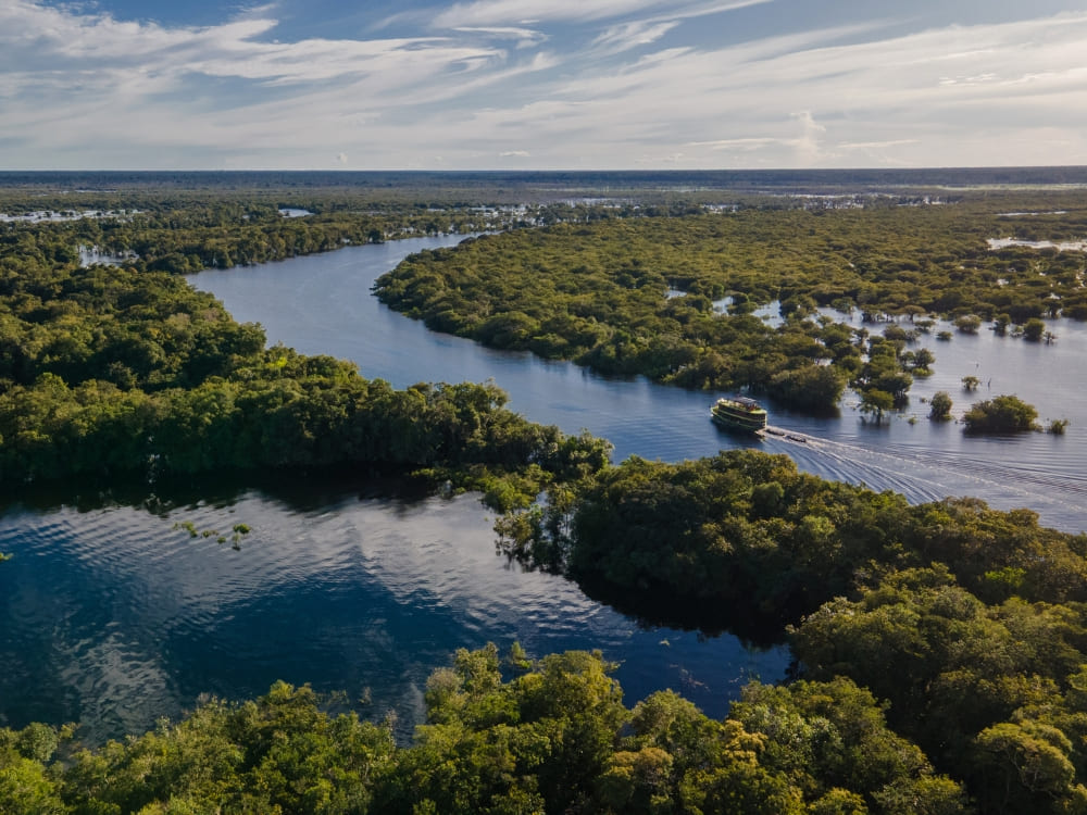 A riverboat navigating a winding channel in the Amazon Rainforest surrounded by thick tropical canopy.