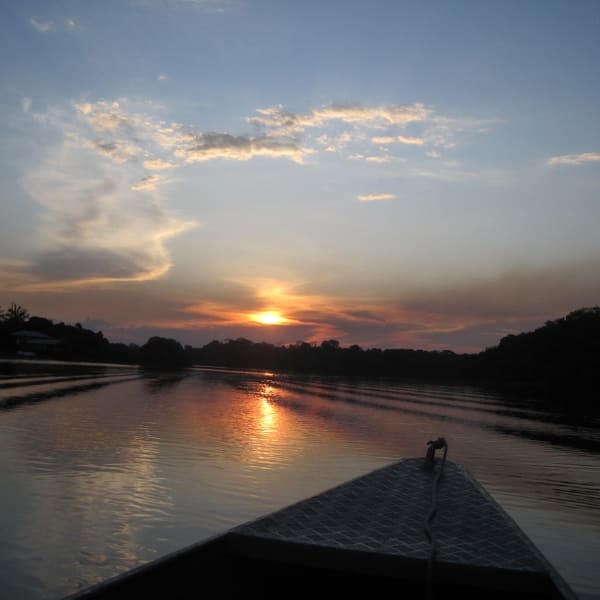 A stunning golden sunset reflects on the calm river waters, viewed from the bow of a small boat during an immersive nature tour in Brazil.