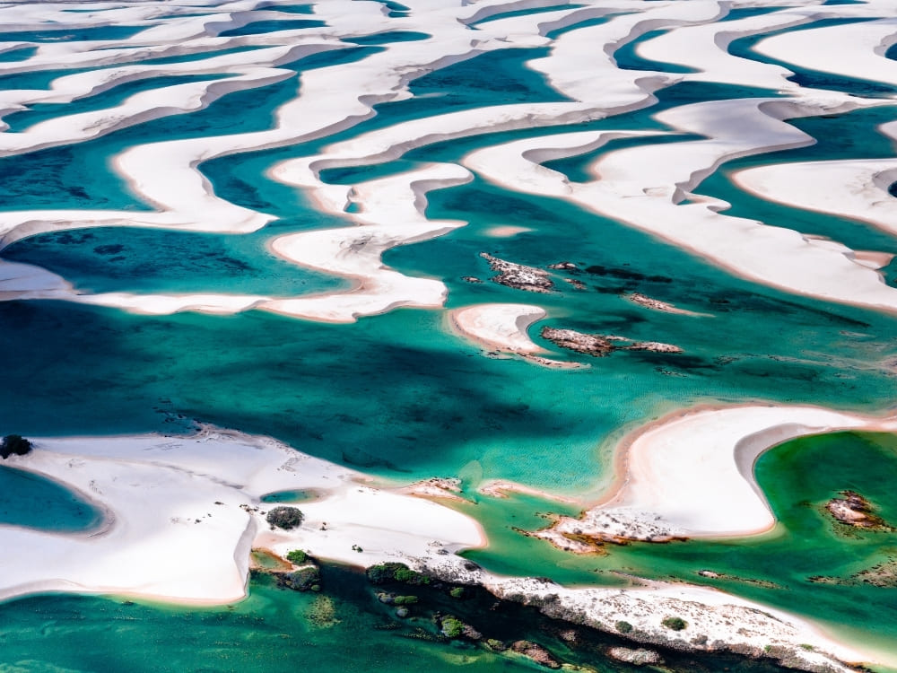 An aerial view reveals expansive, curving white sand dunes filled with vibrant turquoise and dark blue pools of water.