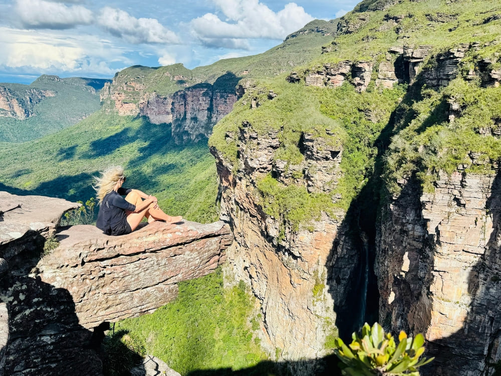  Female adventurer sitting on a rock edge admiring the vast and open green landscapes of Chapada Diamantina. 