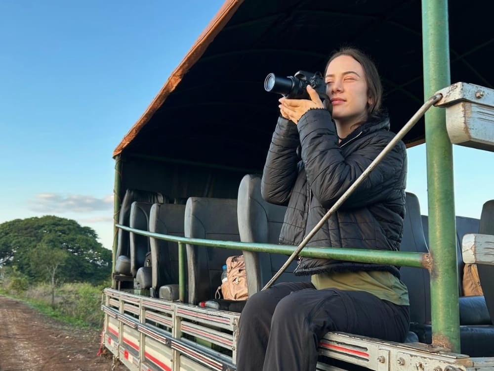 Woman photographing nature from the back of a safari vehicle, illustrating the work of guides and wildlife photographers in ecotourism.