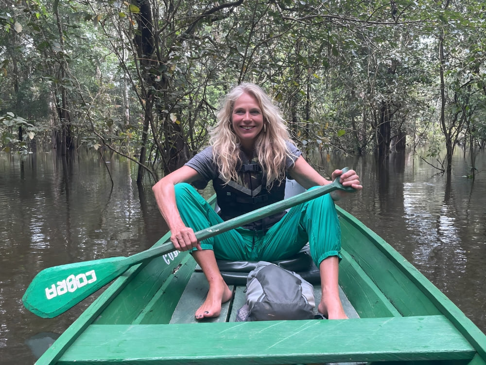Smiling blonde Katharina holding a paddle while navigating a green canoe through a flooded forest in the Amazon.