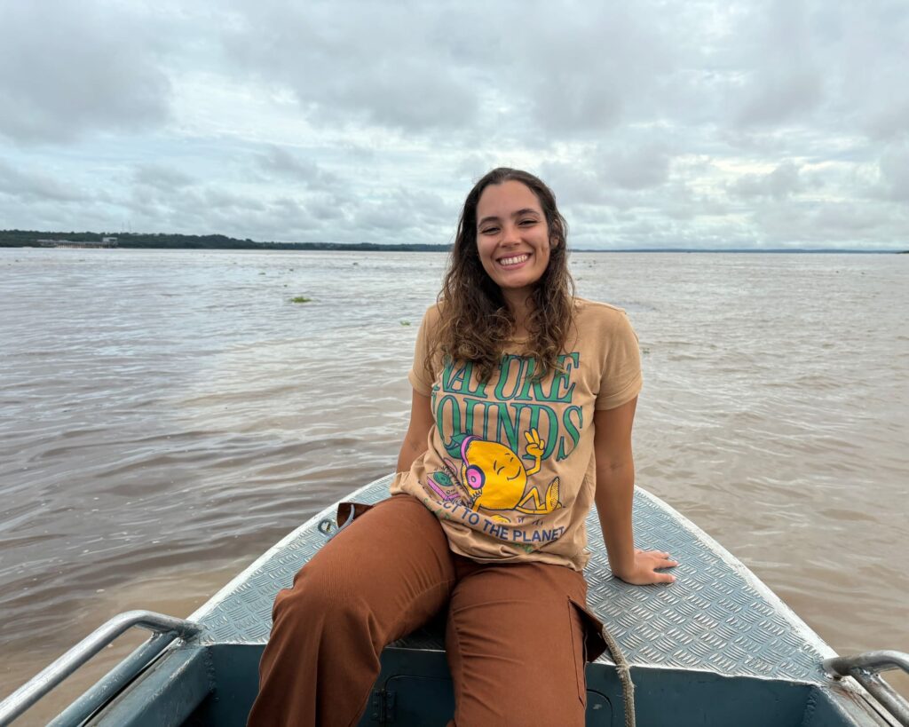 Mariana smiles while sitting on a small boat navigating a wide river during her solo adventure in the Amazon Rainforest.