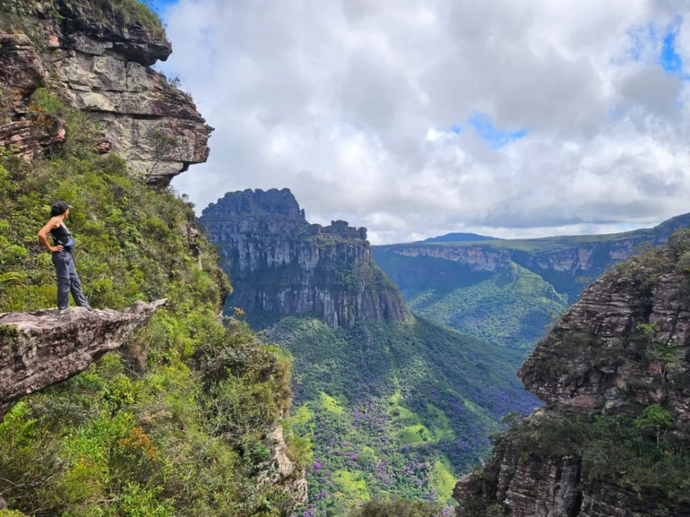 Woman standing on the edge of a rocky cliff admiring mountains and valleys, symbolizing the authentic experiences guided by women in ecotourism.