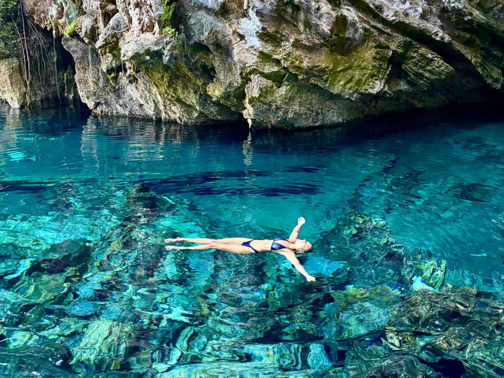  Woman in a bikini floating with open arms in the crystal-clear, turquoise waters of a natural fervedouro surrounded by rocks in Jalapão.