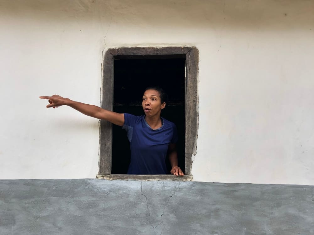 Woman in a blue blouse pointing out the window of a rustic house, representing the female driving force on the front lines of nature travel in Brazil.