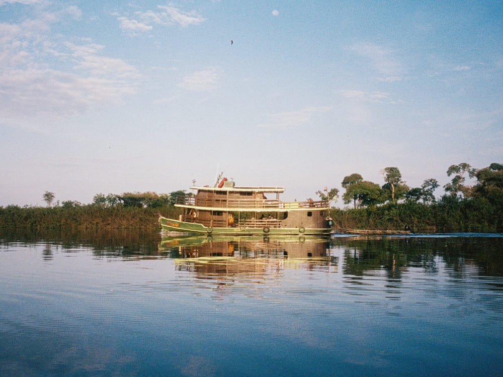 Ein traditionelles Flusskreuzfahrtschiff navigiert auf den ruhigen Gewässern des Rio Negro, während sich die grüne Ufervegetation im Wasser spiegelt.