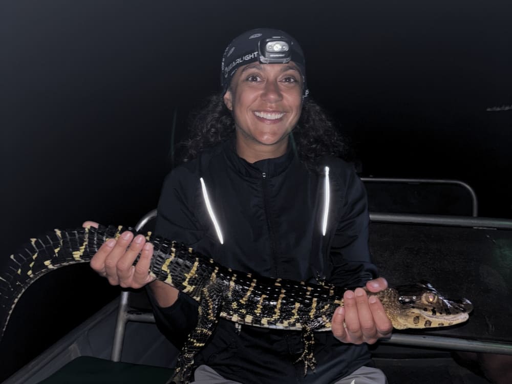 Samantha Sage smiles while holding a small caiman during a guided nighttime ecotourism tour in the Brazilian Amazon.