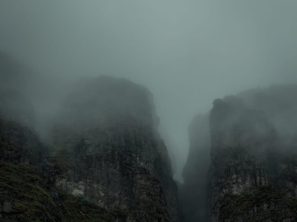 Steep, dark rocky mountain cliffs are partially obscured by thick, gray fog and low-hanging clouds.