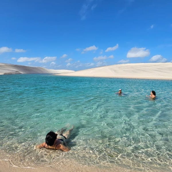 Touristen entspannen sich im flachen, kristallklaren Wasser einer von weißen Sanddünen umgebenen Lagune in Lençóis Maranhenses.