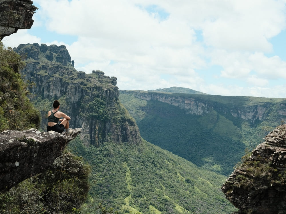  Woman sitting on the edge of a rocky cliff contemplating the green immensity of the plateaus and valleys of Chapada Diamantina.