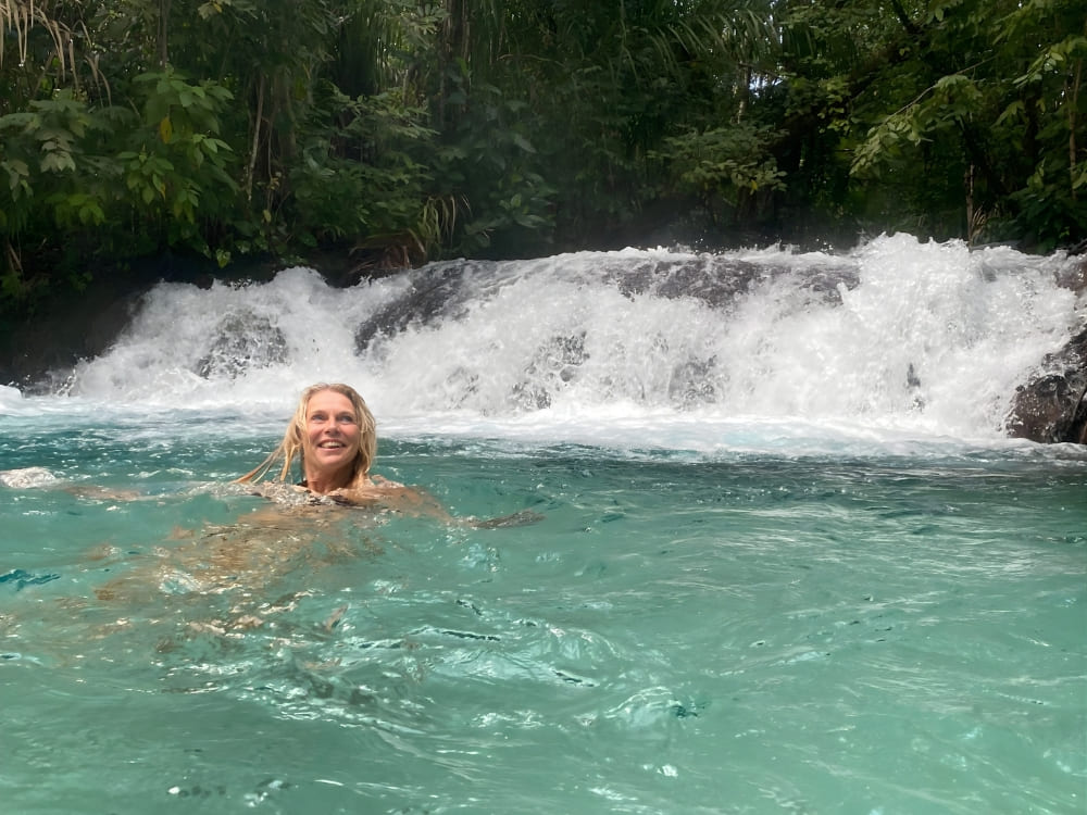  Smiling woman swimming in crystal-clear blue waters with a large waterfall in the background in the Jalapão region.