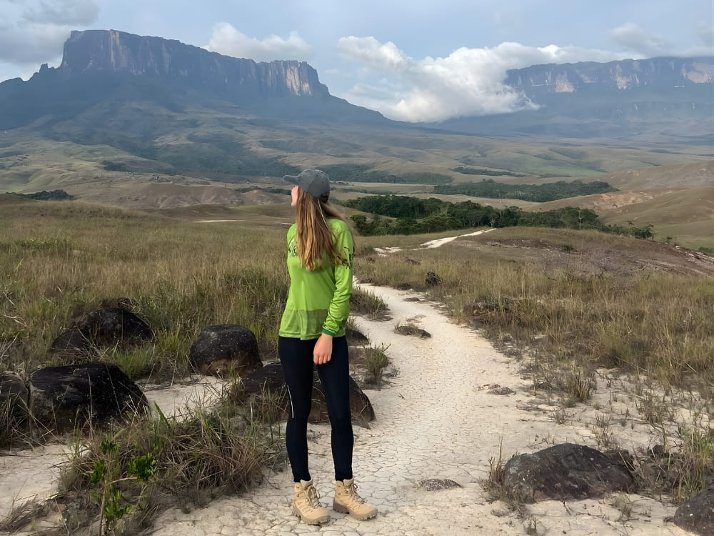  Female ecotourist standing on a dirt hiking trail with the stunning natural wonder of Mount Roraima in the background. 
