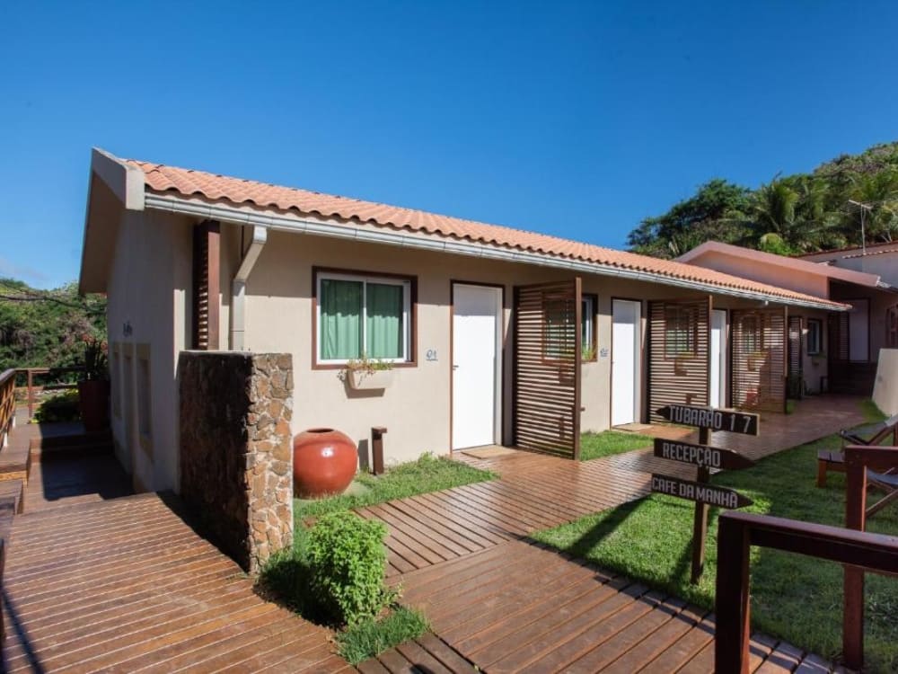 Wooden walkway leading to rustic guesthouse rooms with white doors and small gardens in Fernando de Noronha.