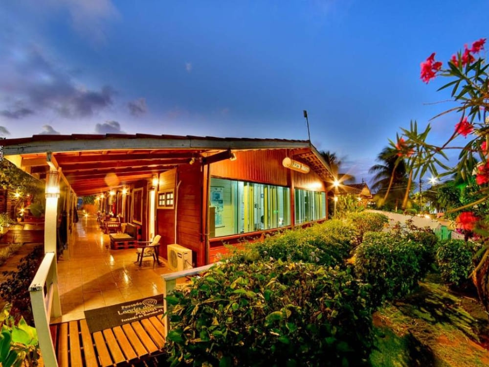 Illuminated rustic pousada exterior at dusk with tropical flowers and a welcoming atmosphere in Fernando de Noronha.