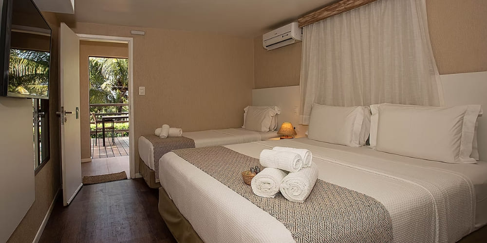 Cozy hotel room featuring a double bed, a single bed, and an open doorway leading to a sunny outdoor balcony in a Fernando de Noronha accommodation.