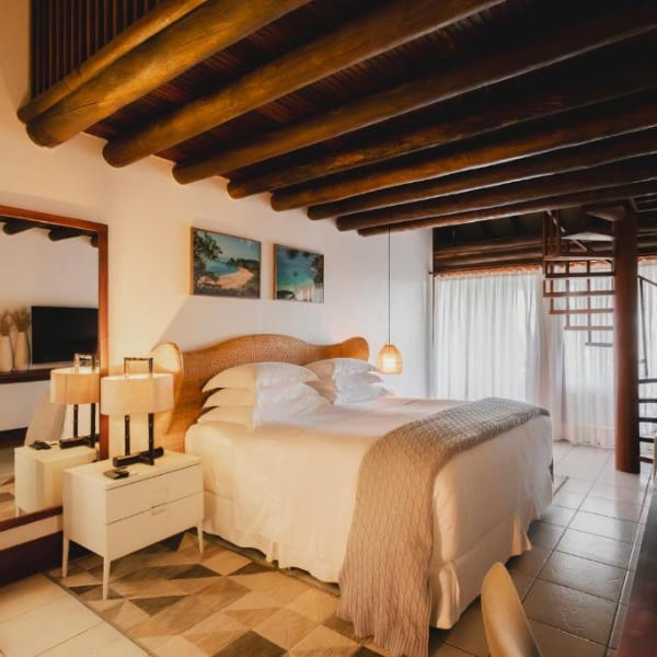 Spacious luxury hotel bedroom with a large bed, rustic wooden ceiling, and elegant natural decor in Fernando de Noronha.