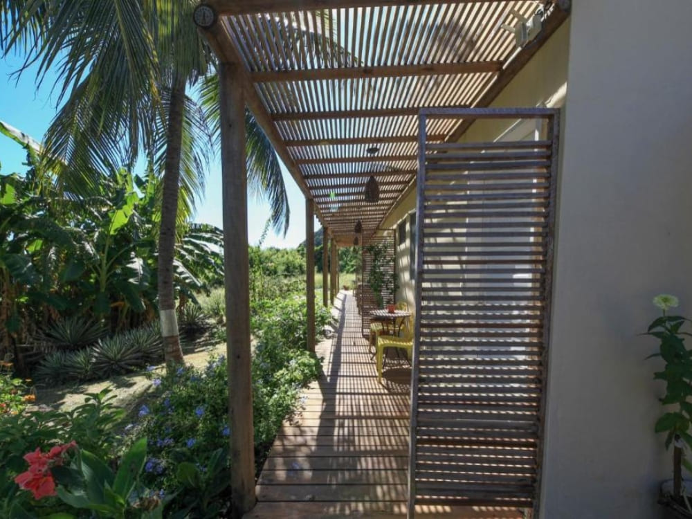 Shaded outdoor corridor with wooden slatted roofing surrounded by green banana plants at a Fernando de Noronha pousada.