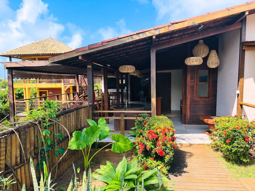 Charmantes Gästehaus-Äußeres mit einer überdachten Veranda, Holzpfeilern und einem grünen tropischen Garten in Fernando de Noronha.