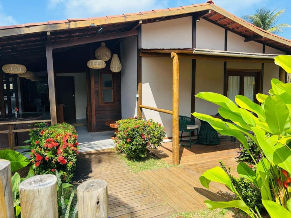 Charming guesthouse exterior featuring a covered porch, wooden pillars, and a green tropical garden in Fernando de Noronha.