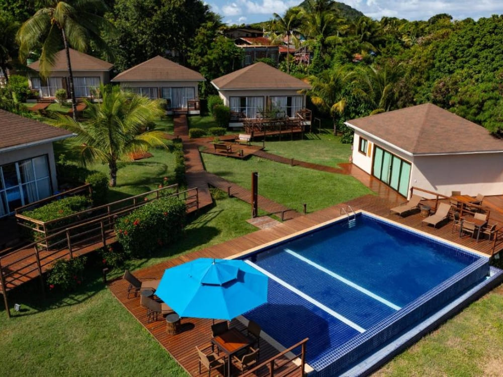 Aerial view of a mid-range guesthouse featuring a blue swimming pool, green lawns, and private cabins in Fernando de Noronha.
