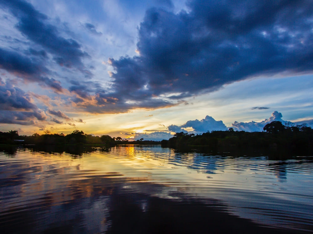 A colorful sunset reflecting on the calm waters of the Amazon River bordered by the rainforest.