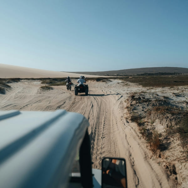 View from behind of people riding quad bikes on a sandy trail toward distant sand dunes in Jericoacoara.