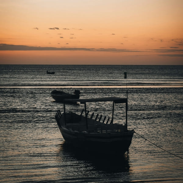 Silhouettes of small wooden boats anchored in calm shallow waters during a golden sunset.