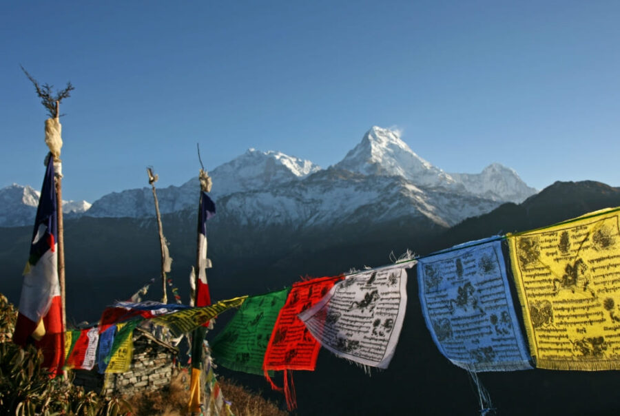 Colorful Tibetan prayer flags fluttering in the wind against the backdrop of the majestic, snow-capped Himalayas , representing the scenic views along the sustainable Mardi Himal trek in the Annapurna region of Nepal.