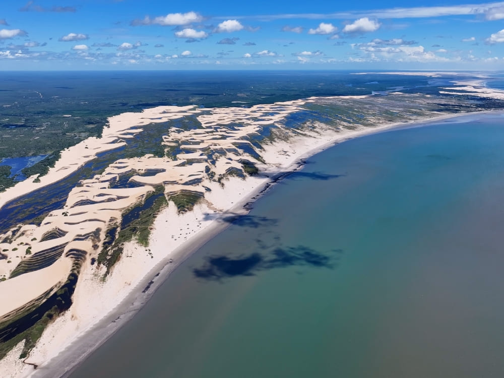 Aerial perspective of the Delta do Parnaiba showing the river branching into the ocean alongside large coastal sand dunes.