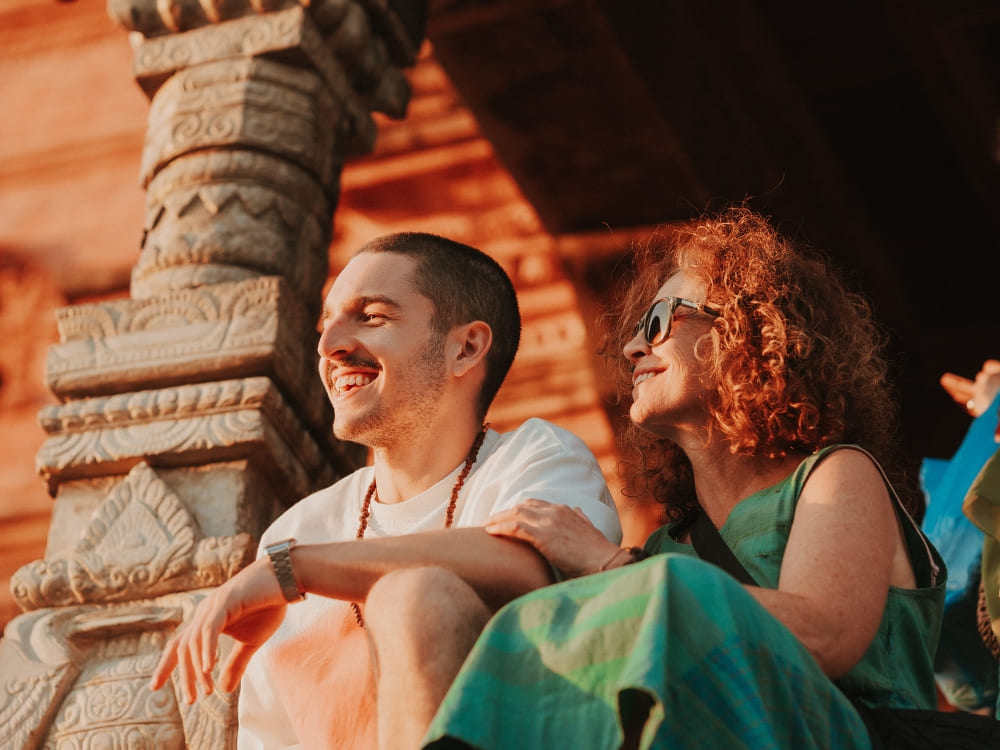 Mila Ricetti and her son Lorenzo smiling and sitting together at a historic brick temple during their ecotourism expedition in Nepal.